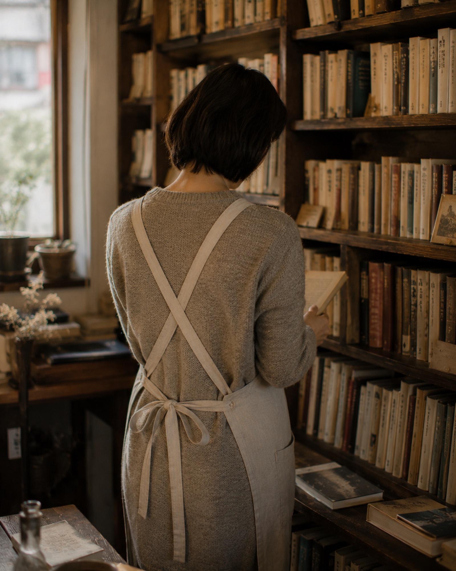 棚の前で本を扱う、PAGES店主の後ろ姿
